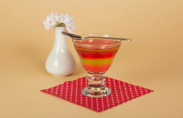 Glass with jelly and a spoon on a napkin, a vase with the flowers, on a beige background — Stock Photo, Image