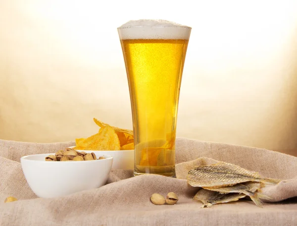 Canvas, glass of beer, pistachio, salty fish and fried potatoes against paper — Stock Photo, Image