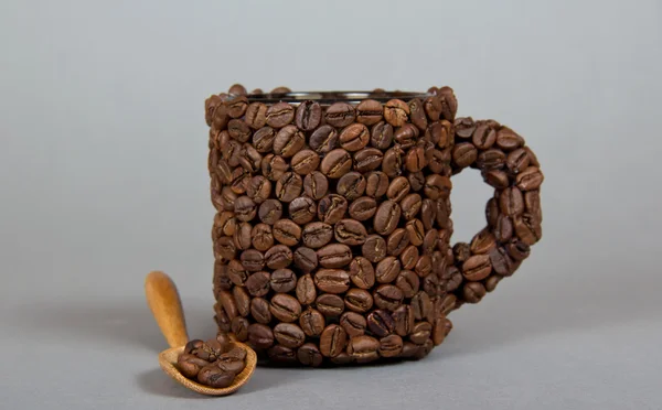 Tasse à café en grains de café, et cuillère en bois, sur un fond gris — Photo