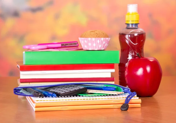 Um jogo de acessórios de escola, garrafa com bebida, bolo e maçã, em uma mesa — Fotografia de Stock