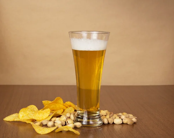 Golden chips, salty pistachios and beer glass against paper — Stock Photo, Image