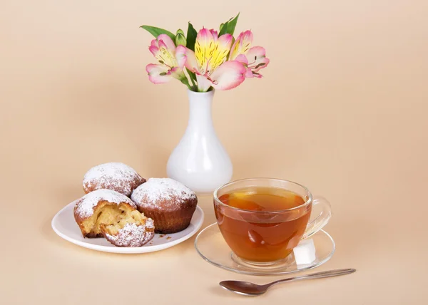 Tea-things, cupcakes and vase with the flowers, on the beige — Stock Photo, Image