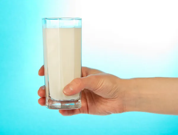 La mano femenina sostiene un vaso lleno de leche sobre un fondo azul —  Fotos de Stock