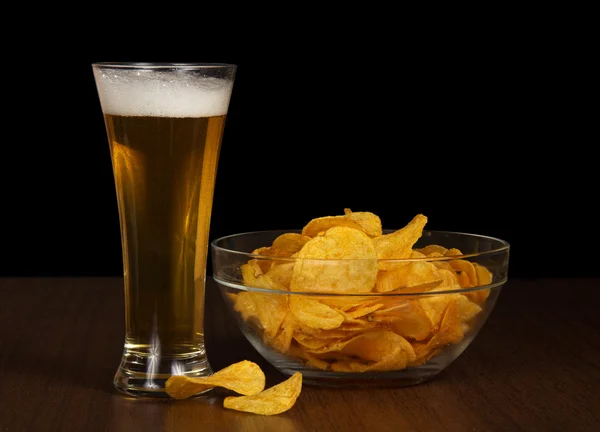 Glass with beer and a bowl with the golden chips, on the table — Stockfoto