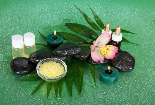 Ensemble d'huiles parfumées, sel, bougies, pierres, une fleur sur une grande feuille, sur un fond vert — Photo
