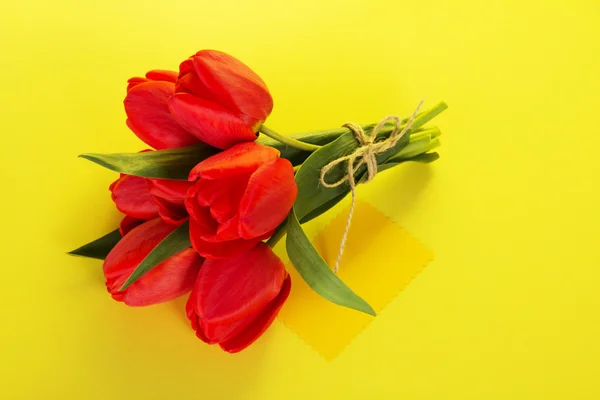 Buquê de tulipas com uma corda e o cartão vazio do texto em um contexto amarelo — Fotografia de Stock