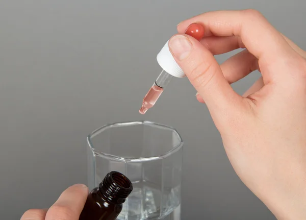 The hand, dripping drops in a glass with water, close up, on a gray background — Stock Photo, Image