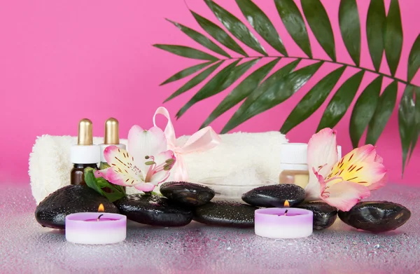 Feuille d'howea sur un ensemble pour une aromathérapie, des bougies et une serviette éponge avec un arc, sur un fond rose humide — Photo
