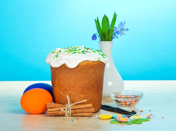 Påsk kaka, ägg, kryddor, en vas med blommor på ett bord, på en blå bakgrund — Stockfoto
