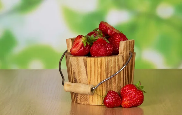 Дерев'яне відро стиглої ароматної полуниці і дві ягоди біля столу — стокове фото