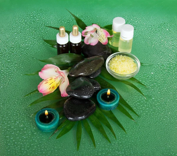 Huile aromatique, sel, bougies, pierres, fleur sur une feuille humide, sur un fond vert — Photo
