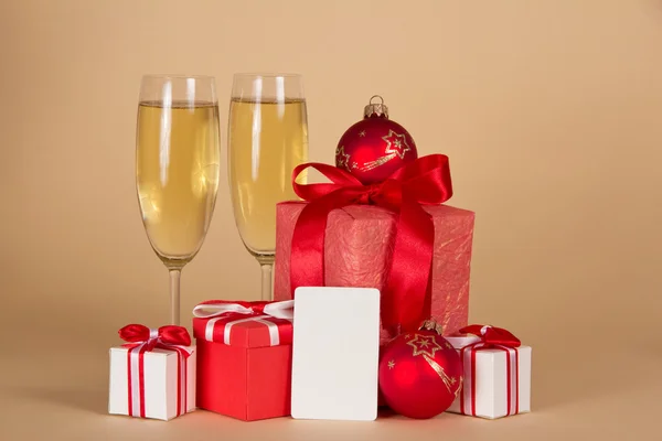 Regalos de Año Nuevo, copas de vino con champán y una tarjeta vacía para el mensaje, sobre un fondo beige —  Fotos de Stock