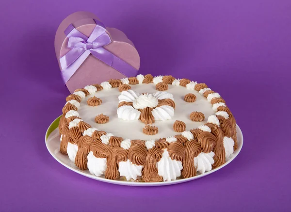 Torta em um prato e um coração de presente em um fundo violeta — Fotografia de Stock