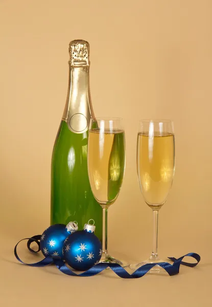 Fles en wijn glazen met champagne, Kerstmis speelgoed en een serpentine op een beige achtergrond — Stockfoto