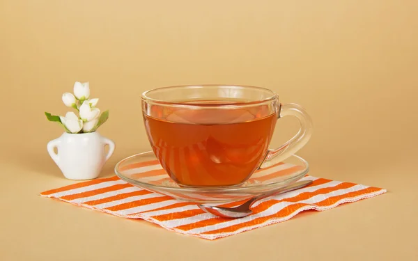 Cup of tea, jasmine in a small vase, a striped napkin, on the beige — Stock Photo, Image