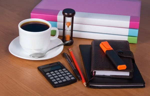Notepad, organizer, marker, folders for documents the calculator, hourglasses and a cup of coffee on a table