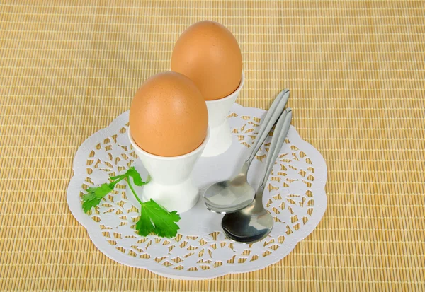 Zwei Eier in einem Ständer und zwei Löffel auf beigem Hintergrund — Stockfoto