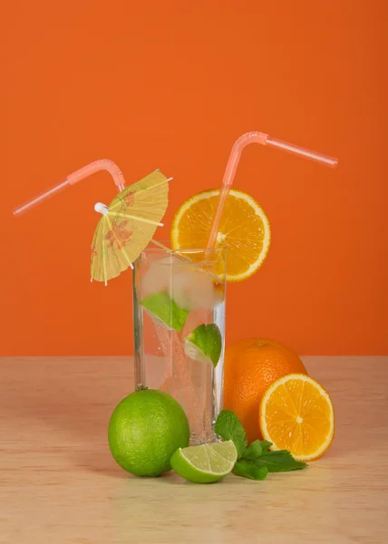 Drink in a glass with straw, is decorated with an umbrella and an orange slice, a juicy lime, on a table — Stock Photo, Image