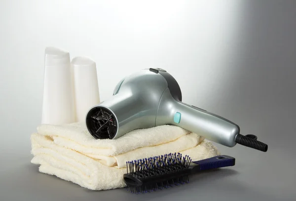Le sèche-cheveux pour les cheveux, une brosse à cheveux et des accessoires de toilette sur fond gris — Photo