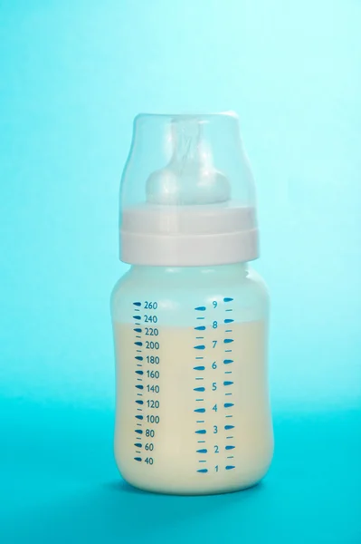 Botella pequeña para niños con leche y chupete sobre fondo azul —  Fotos de Stock