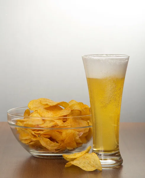 Beer pouring into glass and chips on a gray background — Stock Photo, Image