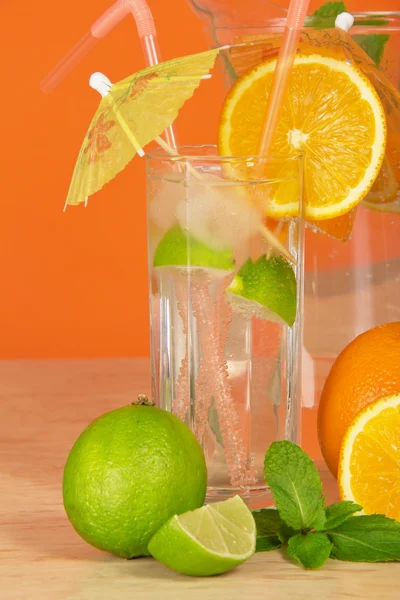 Boire dans un verre avec de la paille, est décoré avec un parapluie et une tranche d'orange, un citron vert juteux, sur une table — Photo