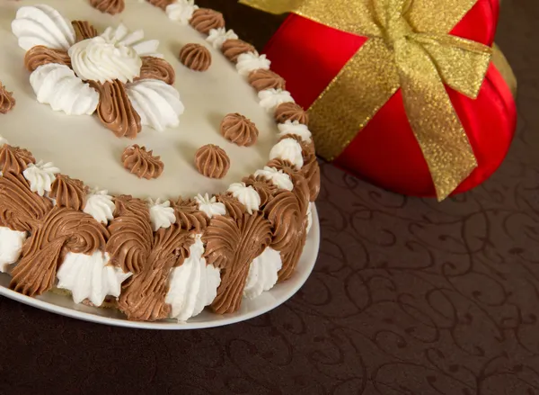 Gateau and the gift box decorated with a tape on a brown cloth — Stock Photo, Image
