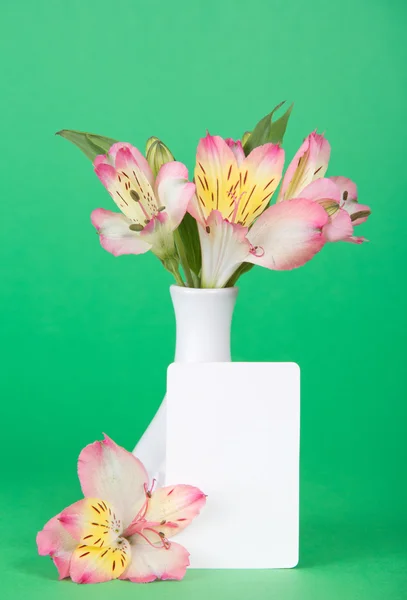 Flor de una alstroemeria y tarjeta vacía cerca de un jarrón, sobre un fondo verde —  Fotos de Stock