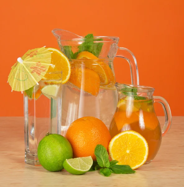 Kannor med drycker, ett glas, en saftig lime och apelsiner på ett bord — Stockfoto