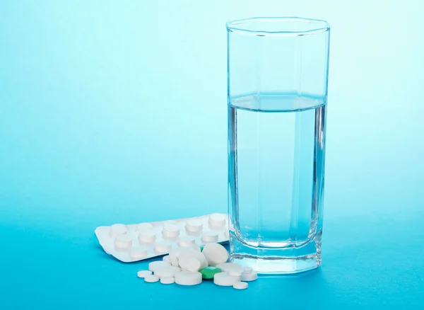 Medicinska preparat och glas med vatten på en blå bakgrund — Stockfoto