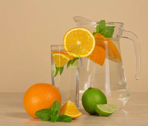 Cruche, verre avec la boisson, décoré avec une tranche d'orange, un citron vert juteux et menthe — Photo