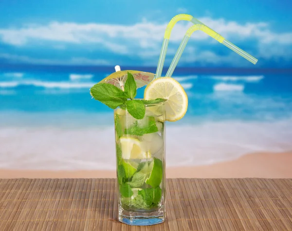 Mojito with cocktail straws and a lemon slice, on a bamboo cloth against the sea — Stock Photo, Image