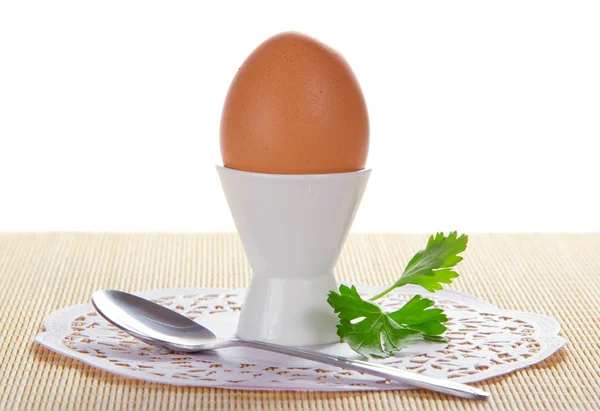 Egg in a support, a spoon, a napkin and greens on the bamboo cloth, isolated on white — Stock Photo, Image