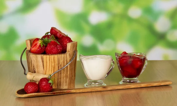 La fresa en el cubo en la taza en la cuchara, y la taza con la crema a la mesa —  Fotos de Stock