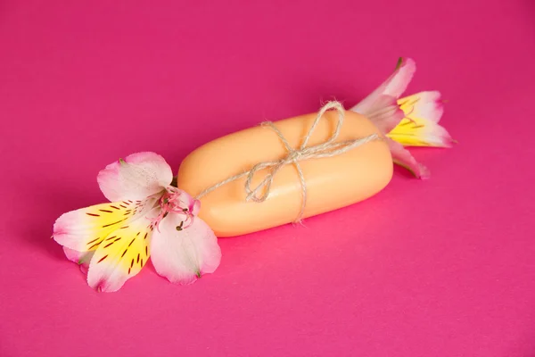 Кусок нового мыла, прикреплённого бечевкой и цветок на розовом фоне — стоковое фото