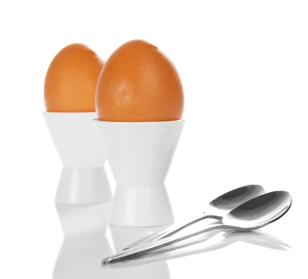 Яйца в опорах и две чайные ложки, изолированные на белом — стоковое фото