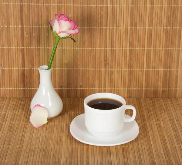 Vase mit einer Rose und einer Tasse mit Getränk gegen ein Bambustuch — Stockfoto