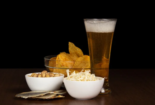Piwo, miska z frytkami, kalmary, pistacje i słone ryby, na stole — Zdjęcie stockowe