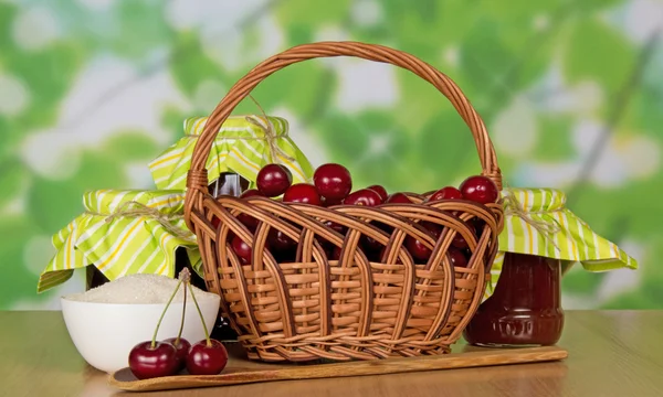 Баночки варення, кошик з солодкими вишнями, чашка з цукром і дерев'яна ложка, на столі — стокове фото