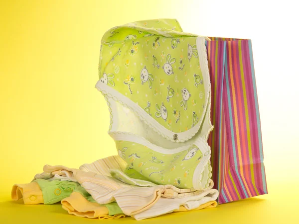 Gift package and baby clothes, on a yellow background — Stock Photo, Image