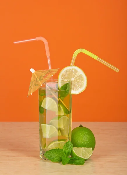 Boire avec une paille, est décoré avec une tranche d'un citron et un parapluie, un citron vert mûr et menthe, sur une table — Photo