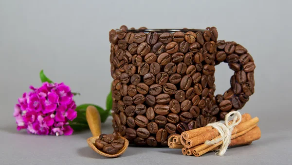 Palitos de canela, la taza hecha de granos de café, cuchara, una rama de clavel brillante — Foto de Stock