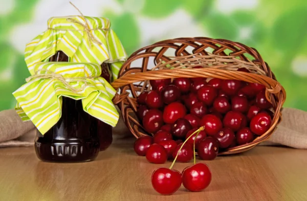 Frascos de engarrafamento, cerejas doces que caíram de um cesto, à frente de uma lona em uma mesa — Fotografia de Stock
