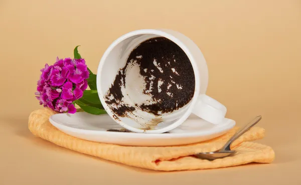 Coffee thick, in the overturned cup, a branch carnation, teaspoon and napkin on a beige background — Stock Photo, Image