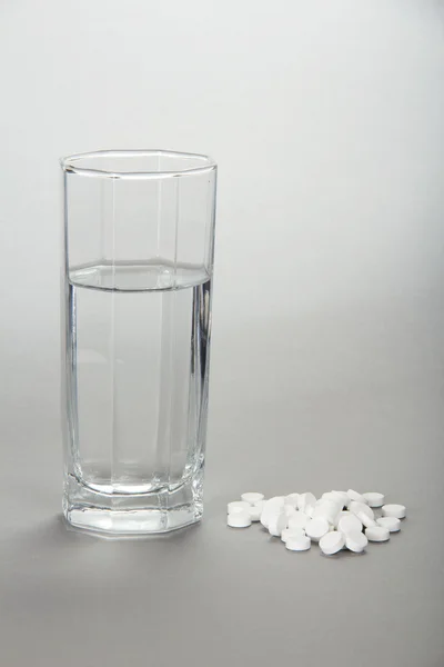 Glass with water and tablets on a grey background — Stock Photo, Image