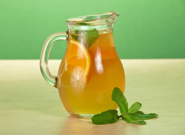 Jarro com bebida cor-de-laranja e hortelã em uma mesa — Fotografia de Stock