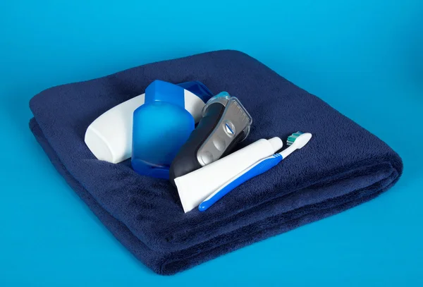 Лосьон, бритва, зубная щетка и зубная паста, махровое полотенце на синем фоне — стоковое фото
