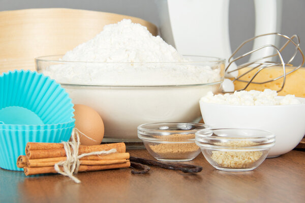 Мука, творог, яйцо, специи и сковородка для торта на столе
