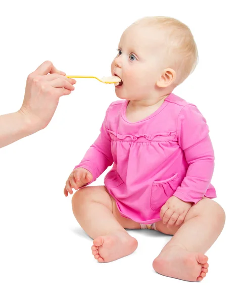 Lief klein babymeisje in een roze jurk eet van een lepel geïsoleerd op wit — Stockfoto