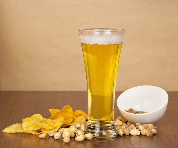 Verre avec de la bière, des chips dorées et les pistaches qui sont tombées d'un bol, contre du papier — Photo